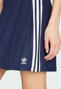 Mornarska atletska haljina s bijelim trostrukim dizajnom sa strane. Sadrži izvezeni bijeli Adidas logo na rubu. Glatka tekstura tkanine.