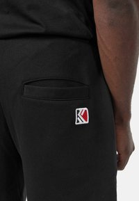 Pantalones jogger de algodón negros con un bolsillo lateral elegante y un pequeño logo bordado en rojo, blanco y azul en la parte posterior.