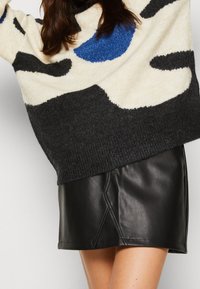 Strickpullover mit einem abstrakten Design in Creme, Blau und Schwarz; kombiniert mit einem eng anliegenden schwarzen Leder-Minirock mit diagonalen Nähten.