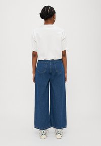White cotton t-shirt with short sleeves, paired with wide-leg blue denim pants and white sneakers, viewed from the back.
