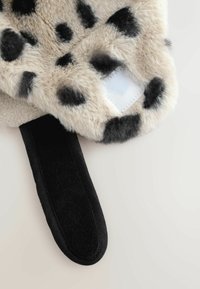 Faux-Fur-Hausschuhe mit einem beigen und schwarzen gepunkteten Design, einer schwarzen Filzsohle und einem weißen Stoffeinsatz auf der Oberseite.