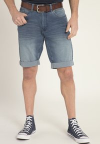 Shorts in denim azzurro, con orli arrotolati e tasche anteriori, abbinati a sneaker alte nere e una cintura marrone. Texture liscia.