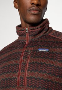 Red and black patterned fleece pullover with a high collar, half-zip closure, and Patagonia logo on the chest; soft texture and knitted design.