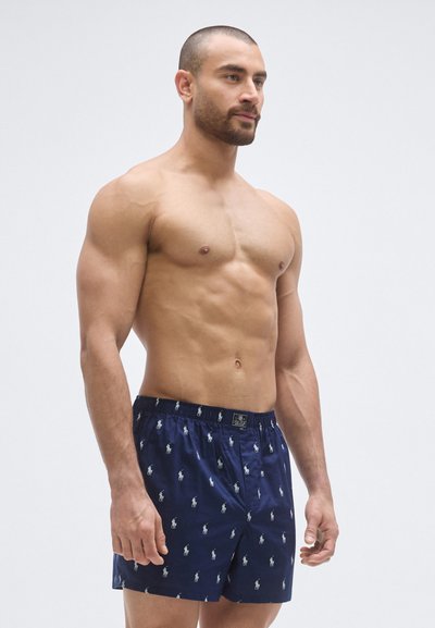 Námornícka modrá boxerky z ľahkej látky s opakujúcim sa vzorom bieleho hráča póla. Elastický pás so štítkom s logom.