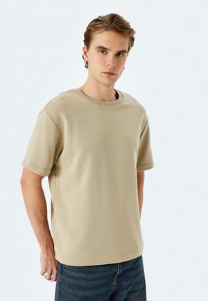 Camiseta de manga corta beige con escote redondo. Fabricada en una suave mezcla de algodón, presenta un corte relajado y mínimas costuras.