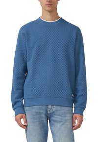 Niebieska teksturowana bluza z wzorzystą tkaniną, z okrągłym dekoltem i ściągaczami na rękawach. Do tego jasnoniebieskie dżinsy.