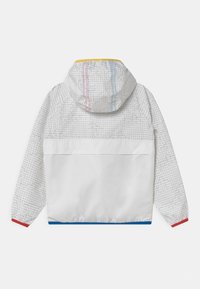 Vit jacka med ett mönstrat grått övre parti, huva och elastiska ärmslut. Har röda och blå detaljer vid fållen och ärmsluten.