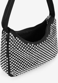 Bolso de tela negra con forma curva, adornado con tachuelas plateadas en un patrón de degradado y un cierre de cremallera en la parte superior.
