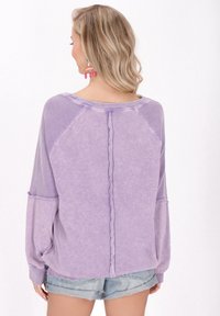 Pulover mare, de culoare purpurie, cu accente ribbed, textură moale și mâneci raglan. Are o cusătură centrală și o croială lejeră. Asortat cu pantaloni scurți din denim.