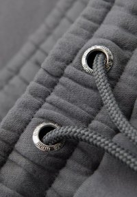 Grauer Stoff mit strukturierter Oberfläche. Verfügt über silberne Ösen und einen grauen geflochtenen Kordelzug. Nahaufnahme zeigt die Nähdetails.