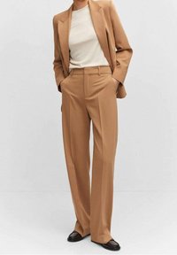 Blazer beige et pantalon large assorti, fabriqués en tissu lisse avec une coupe ajustée. Un haut simple de couleur claire en dessous.