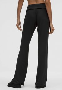 Fekete, bő szabású nadrágok, puha anyagból, magas, rugalmas derékrésszel. Simább textúra, látható minták vagy fémrészek nélkül.