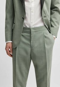 Light green suit with a textured fabric, featuring a single black lapel, flat front trousers, and a white button-up shirt underneath.