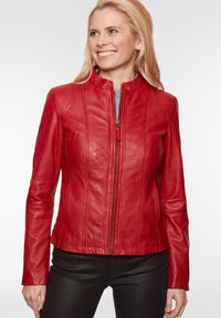 Rote Lederjacke mit Reißverschluss, hohem Kragen und vertikalen Nahtdetails. Weicher Stoff, taillierte Passform und lange Ärmel. Schwarze Hose.