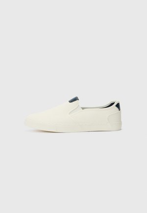 Sapatos slip-on feitos de tecido branco leve com uma superfície texturizada e um acento de calcanhar escuro em contraste. Sola de borracha para aderência.
