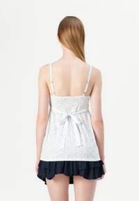 White floral top with adjustable straps and a gathered waist, paired with a dark navy ruffled skirt. Smooth fabric texture and subtle pattern.