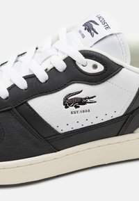 Baskets Lacoste blanches et noires avec lacets blancs, logo crocodile, texte "EST.1933" et semelle rembourrée.