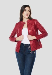 Červená kožená bunda s diagonálnym prešívaným vzorom, golierom so cvokmi a priliehavým strihom. Modelka ju kombinuje s bielym topom a vyšívanými džínsami.