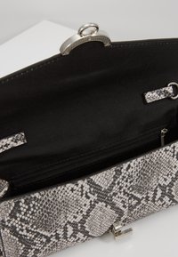 Kabelka na ruku s černobílým hadím vzorem, kovovými doplňky a hladkým černým interiérem. Obsahuje zipovou kapsu a očko.