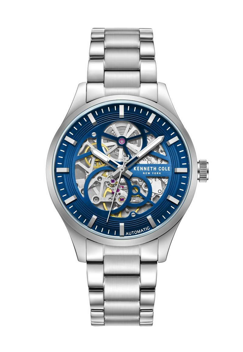Automatyczny zegarek ze stalowej bransoletki. Niebieska tarcza z widocznym mechanizmem ma ażurowy wzór, białe znaki godzinowe oraz złote akcenty.