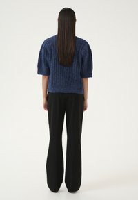 Maglione lavorato a maglia blu con maniche corte e texture a coste, abbinato a pantaloni larghi neri. Design semplice e moderno.