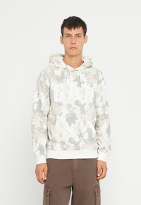 Felpa bianca con stampa di foglie in tonalità di grigio e beige, con il logo "GAP" in bianco ben visibile e una tasca frontale.