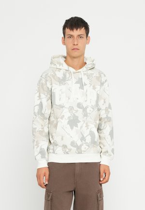 Weißer Kapuzenpullover mit einem Blätterdruck in Grautönen und Beige, mit einem auffälligen weißen "GAP"-Logo und einer Fronttasche.