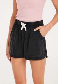 Shorts neri in denim con vita elasticizzata, cordino bianco, tasche laterali e vestibilità comoda. Tessuto morbido con una leggera sfumatura.