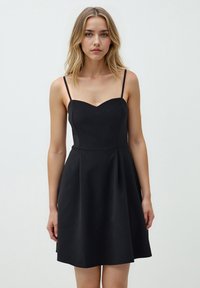 Zwarte mouwloze jurk met een hartvormige halslijn, een getailleerde corsage en een uitlopende rok. Gemaakt van gladde stof met dunne bandjes.