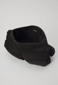 Black corduroy bag with a rounded shape, zip closure, and a soft texture. Features a small inner pocket labeled "YOURTURN."