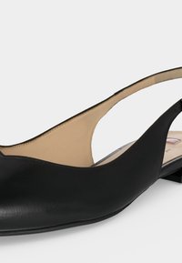 Zapato plano slingback de cuero negro con tacón bajo y forro interior beige, mostrado sobre un fondo liso gris claro.