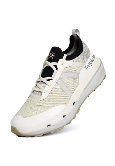 Baskets de sport beige clair avec un upper en maille texturée, une semelle intermédiaire blanche épaisse et une semelle en caoutchouc. Présente des accents noirs et gris ainsi qu'un logo.