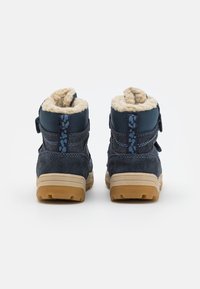 Botines de ante azul con forro de piel sintética, suela de goma y correa ajustable con cierre de gancho y bucle. La parte trasera cuenta con un detalle texturizado en color marino.
