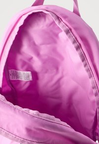 Ανοιχτό ροζ σακίδιο πλάτης που δείχνει το κενό εσωτερικό με μικρή λευκή ετικέτα φροντίδας κοντά στο άνοιγμα του φερμουάρ.