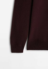 Viininpunaisen neuleen yksityiskohta, jossa on pehmeä tekstuuri, resorit hihansuissa ja helmassa, yksinkertaisella ja klassisella designilla. Lähikuva hihasta.