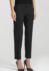 Czarne, dopasowane spodnie wykonane z gładkiej tkaniny, o wąskim kroju z prasowanymi szwami i skróconej długości, zestawione z czarnymi szpilkami.