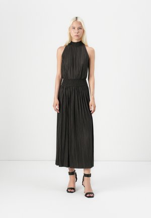 Svart plissert kjole med halterneck, smocket midje og flytende skjørt. Kombinert med svarte strappy høye hæler. Glatt tekstur.