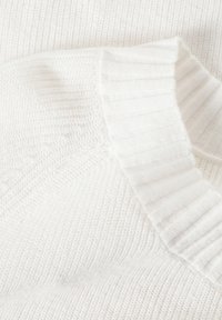 Hvid strikket sweaterstof med en ribbet krave og en struktureret krop. Overfladen har et fint mønster med varierende stingdetaljer.