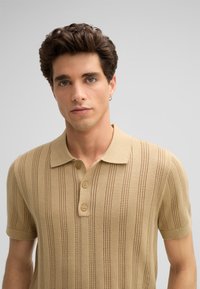 Beige gebreide polo shirt met verticale strepen en een drieknoopsluiting. Korte mouwen en geribbelde textuur met knoopdetails.