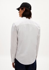 Witte lange mouw shirt met een rechte snit, met knoopmanchetten, rug yoke detail, gedragen met een zwarte pet en heeft een gladde textuur.
