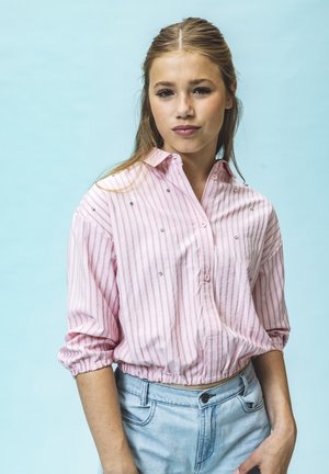 Lichtroze gestreepte overhemd met opgerolde mouwen en decoratieve rhinestones. Drachtig met lichtblauwe high-waisted jeans.