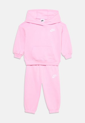 Lyserødt Nike sæt til småbørn med hvidt logo på bryst og ben, vist på hvid baggrund.