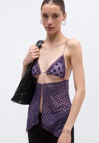 Lilla läbipaistev pluus lilla täpilise mustri, pitsiliste servade, kolmnurksete tasside ja ees oleva võtmeauguga, mille juurde kuulub läikiv must kott.