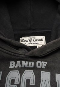 Tummanharmaa huppari, jossa on pehmeä tekstuuri, ja etuosassa suuri painettu teksti "BAND OF RASCALS" vaaleanharmaana. Tagi näkyvissä.