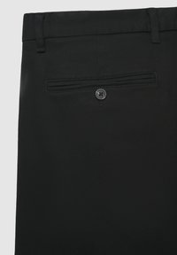 Pantaloni neri con una finitura testurizzata, dotati di una tasca posteriore singola con chiusura a bottone e passanti per la cintura in vita.