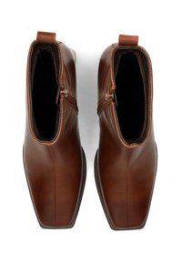 Par de botas cortas de cuero marrón con cremalleras laterales y punteras cuadradas, vistas desde arriba sobre un fondo blanco.