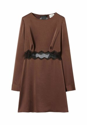 Femme portant une mini-robe marron à manches longues avec un détail en dentelle noire à la taille, tenant un sac à main beige et portant des bottes hautes en daim marron.