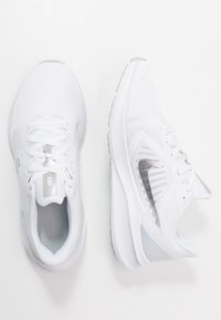 Pár bílých prodyšných síťovaných běžeckých bot se stříbrným logem Nike swoosh, přičemž jedna ukazuje pohled shora a druhá z boku na bílém pozadí.