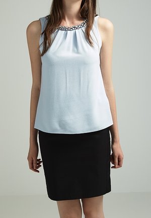 Blouse bleu clair sans manches avec un col orné de bijoux, associée à une jupe crayon noire longueur genou portée par une personne debout.