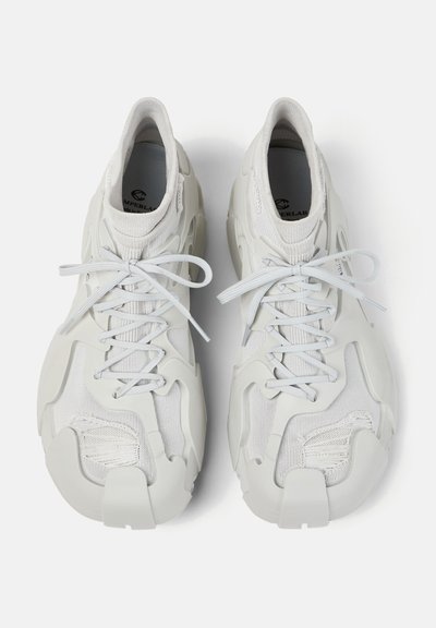 Paire de baskets futuristes blanches avec dessus en tricot, semelle épaisse et fermeture à lacets, vues de dessus sur fond blanc.